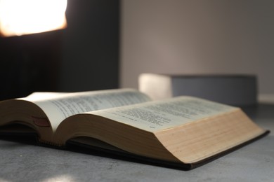 Closeup view of open hardcover Bible on grey table indoors, space for text. Religious book