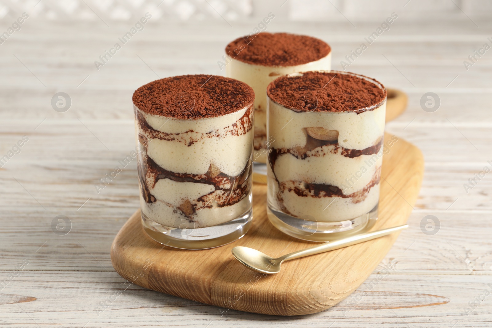 Photo of Delicious tiramisu in glasses and spoon on light wooden table