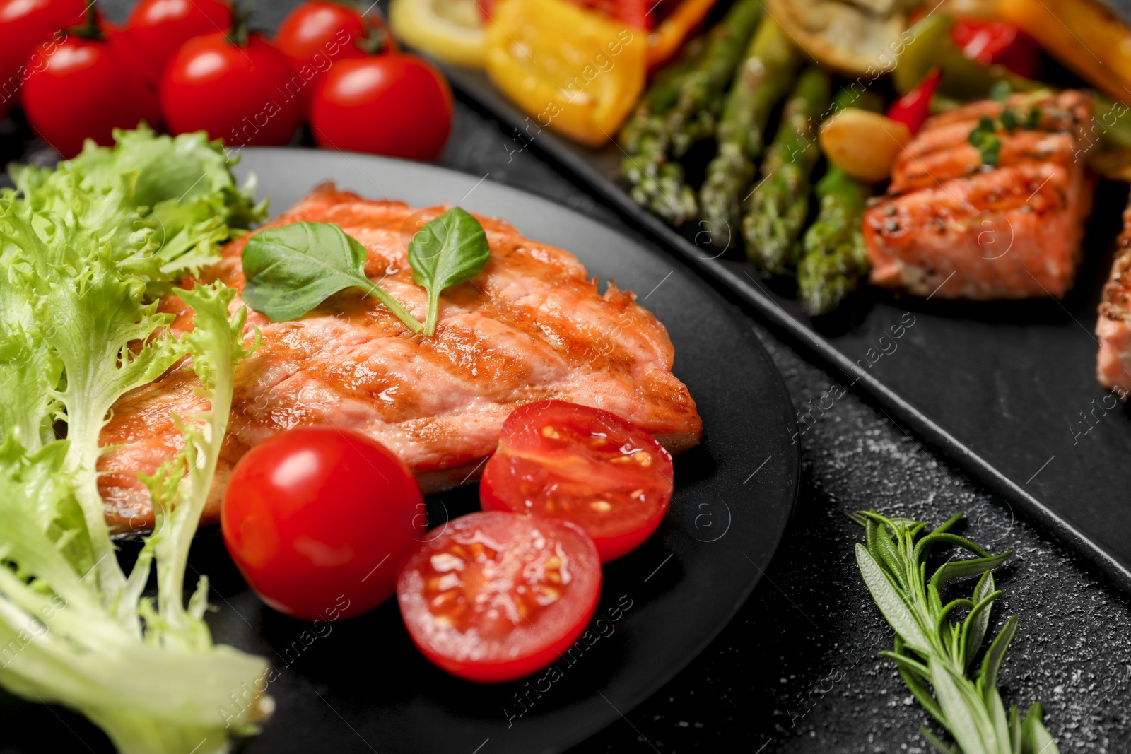 Photo of Tasty grilled salmon with tomatoes and fresh lettuce on black table, closeup. Space for text