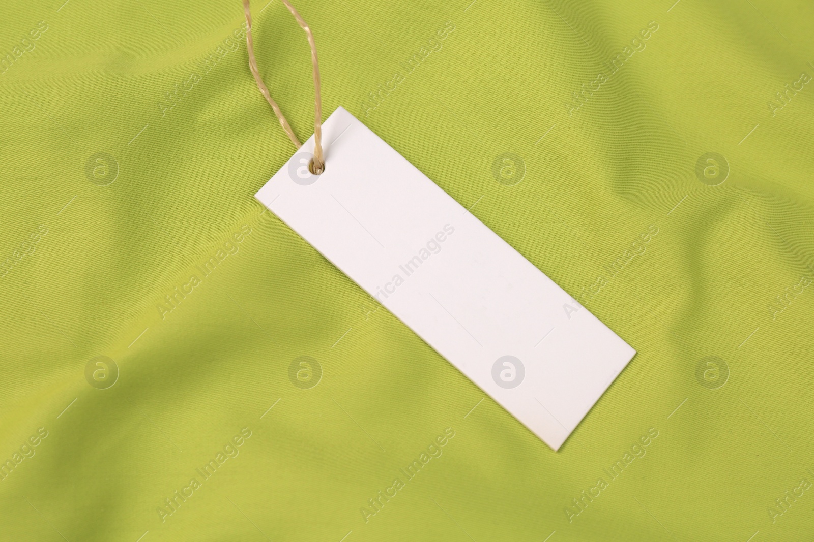 Photo of Blank white tag on green fabric, top view. Space for text