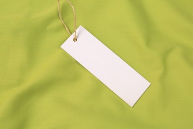 Photo of Blank white tag on green fabric, top view. Space for text