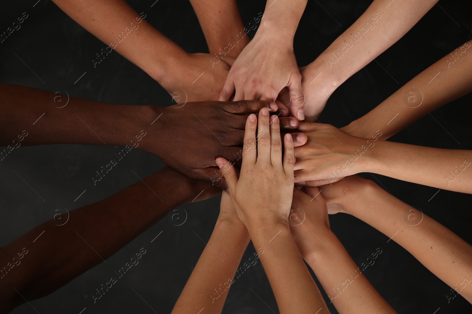 Photo of Group of multiracial people joining hands together on black background, closeup