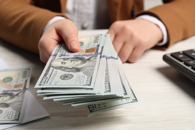 Money exchange. Woman holding dollar banknotes at white wooden table, closeup