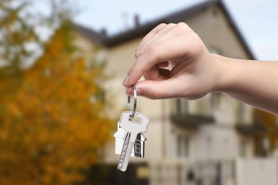 Woman holding key near house outdoors, closeup