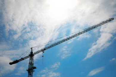 Photo of Modern tower crane at construction site against blue sky, low angle view
