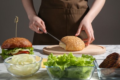 Photo of Woman making delicious vegetarian burger at white marble table, closeup