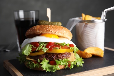 Tasty burger with fried egg on board against dark background