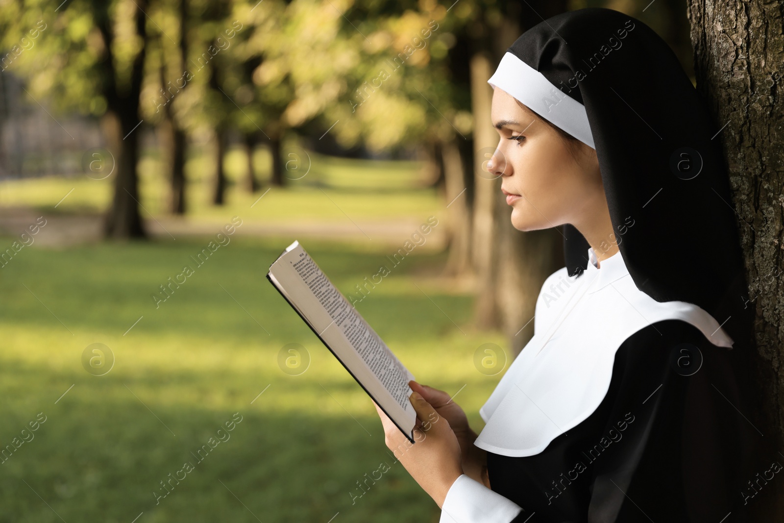 Photo of Young nun reading Bible in park on sunny day, space for text