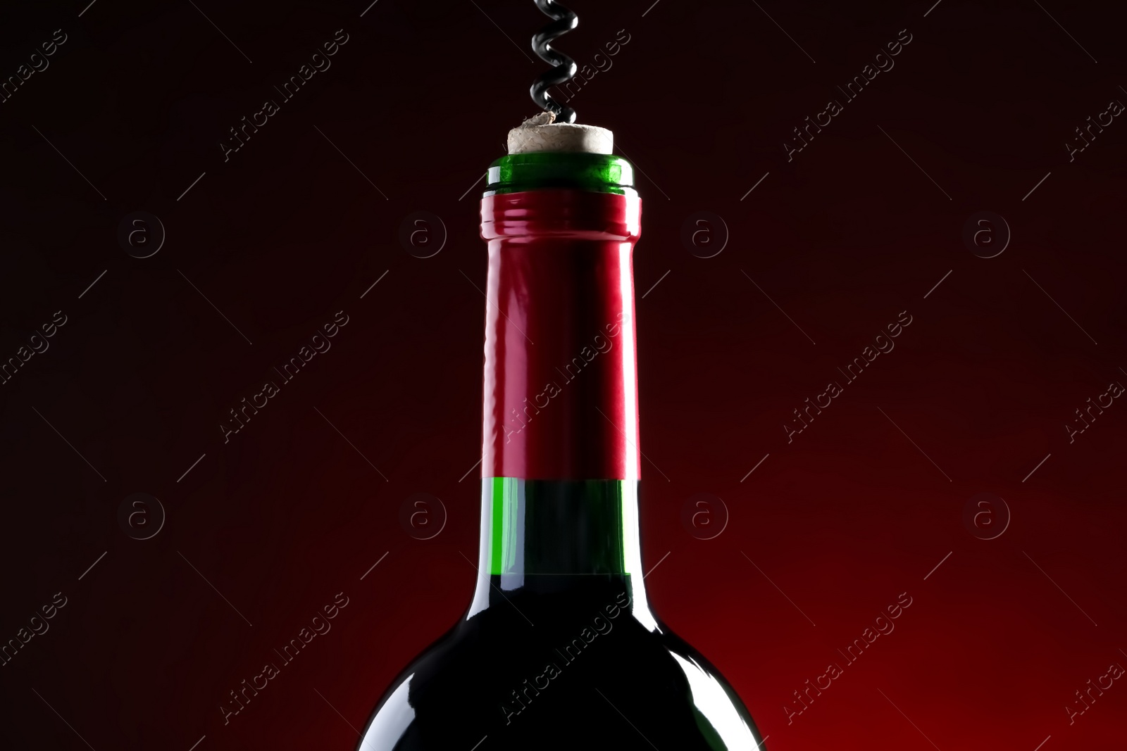 Photo of Opening wine bottle with corkscrew on dark red background, closeup