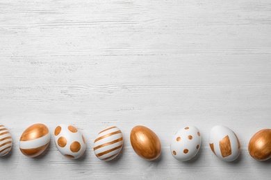 Photo of Set of traditional Easter eggs decorated with golden paint on wooden background, top view. Space for text