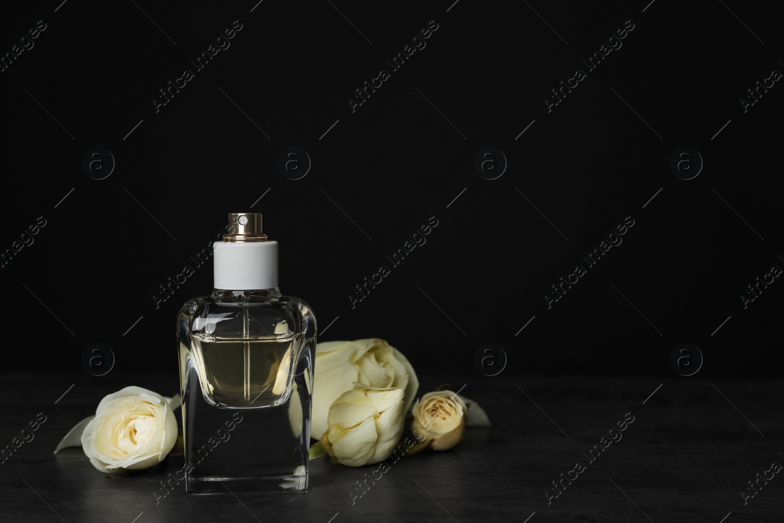 Photo of Perfume bottle and flowers on table against black background