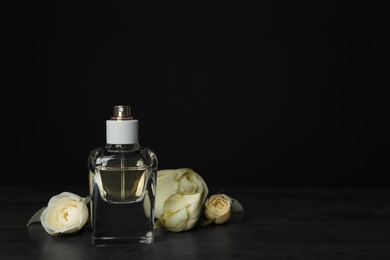 Perfume bottle and flowers on table against black background