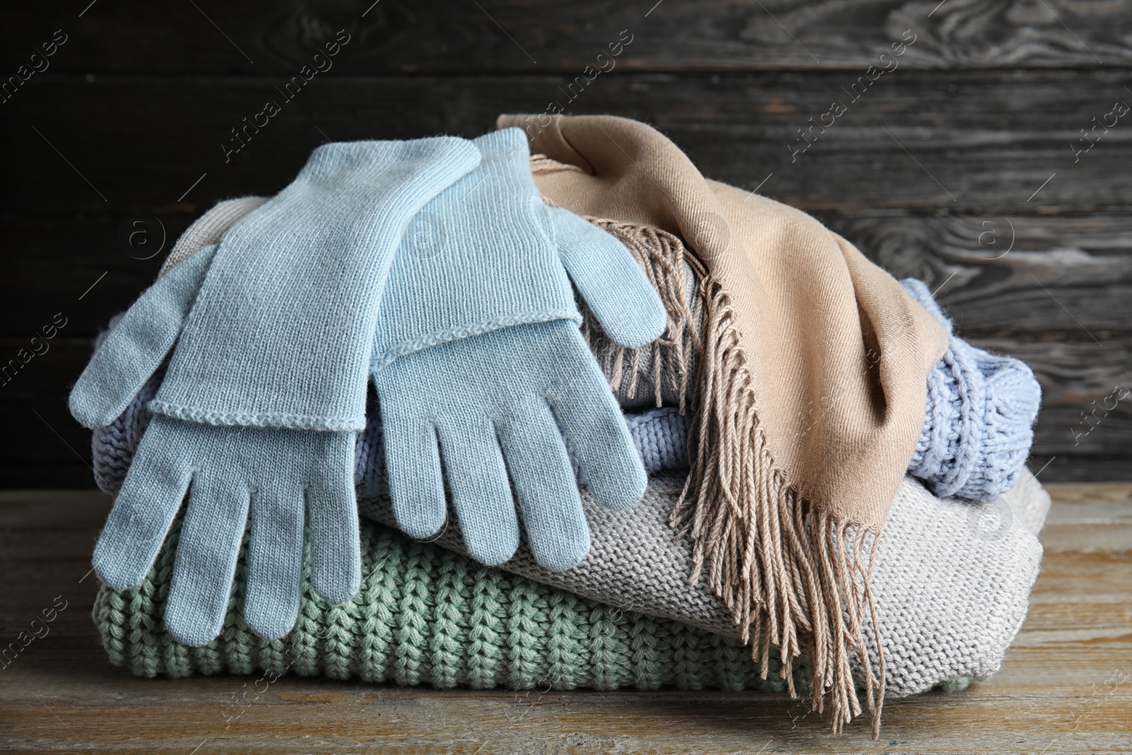 Photo of Stacked sweaters and gloves on wooden table, closeup. Autumn clothes