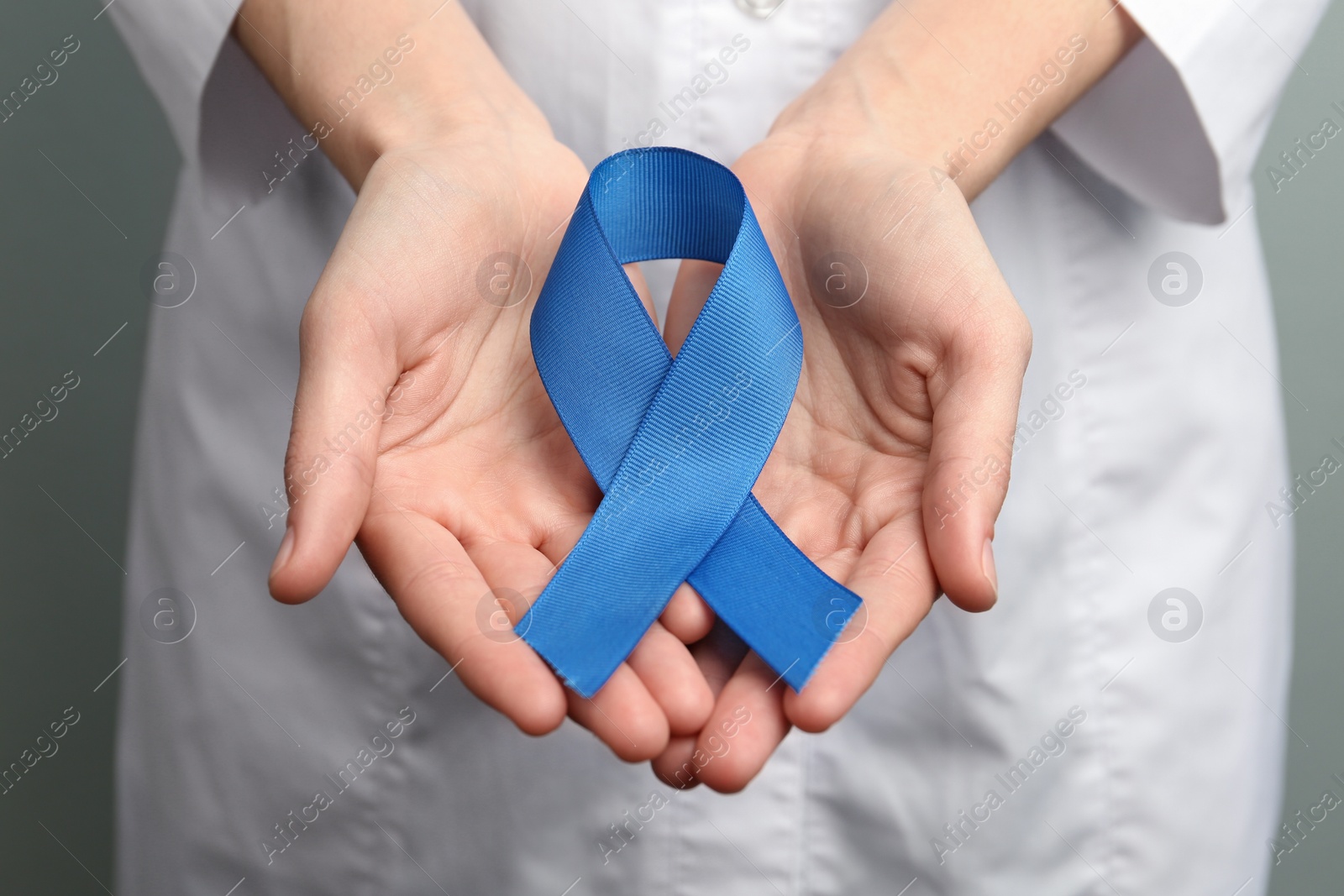 Photo of Doctor holding blue awareness ribbon, closeup view. Symbol of medical issues