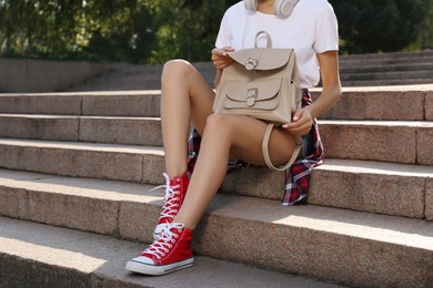 Young woman with stylish beige backpack on stairs outdoors, closeup