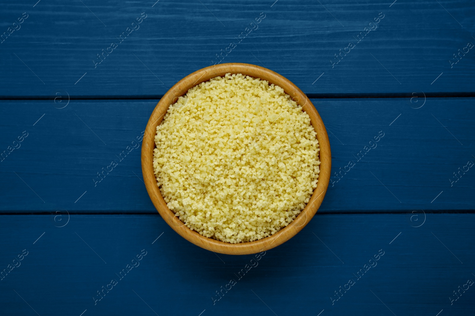 Photo of Bowl of tasty couscous on blue wooden table, top view