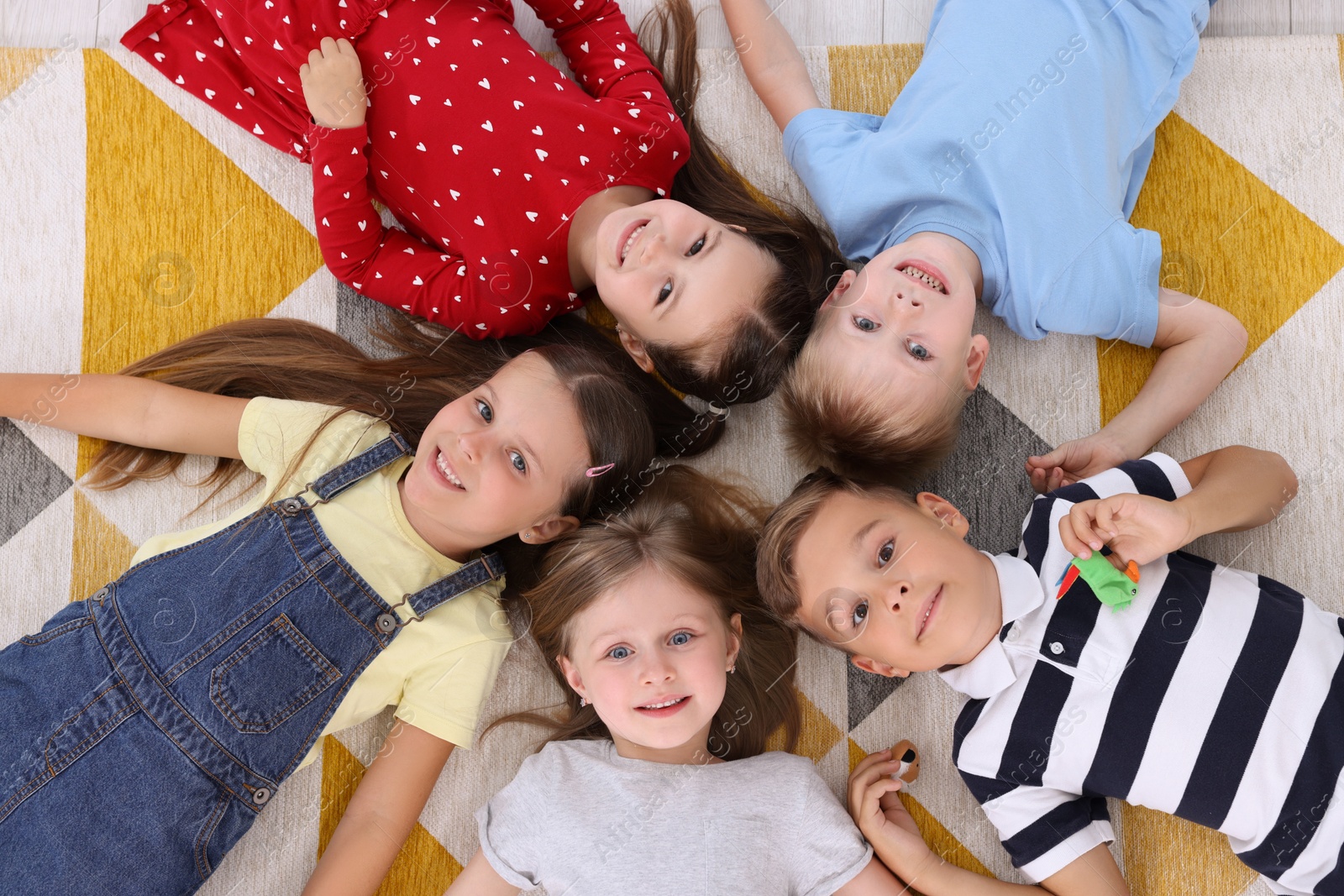 Photo of Adorable little children lying on bright carpet together in kindergarten, top view. Playtime activities