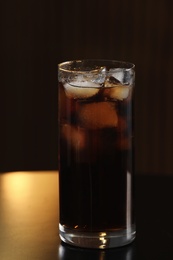 Photo of Glass of cola with ice on table against blurred background