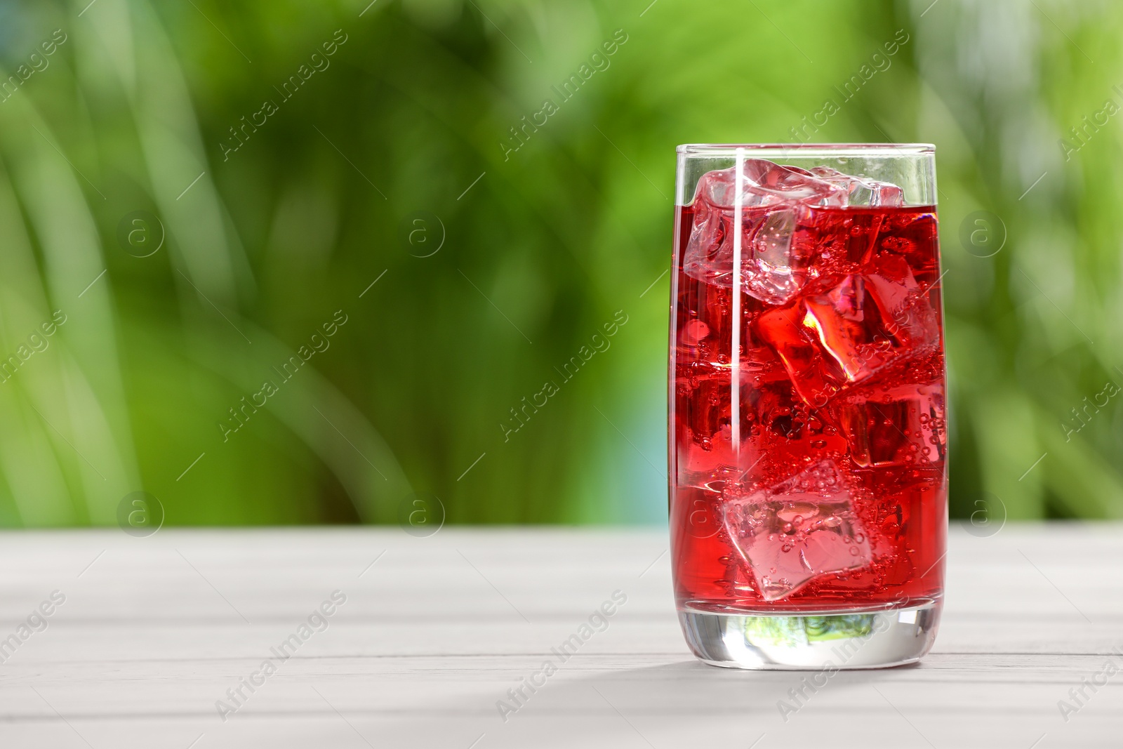 Photo of Glass of refreshing soda water with ice cubes on white table outdoors, space for text