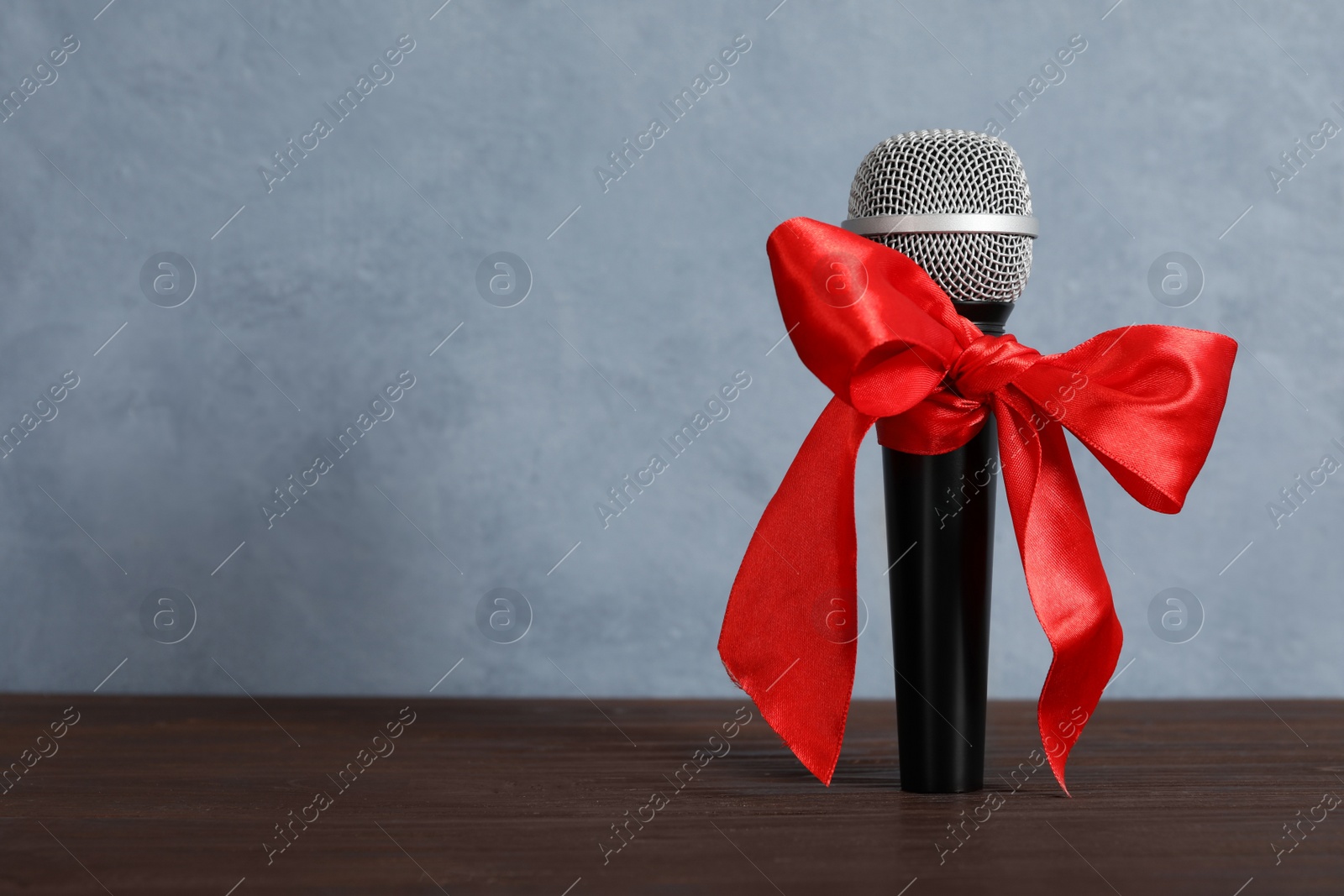 Photo of Microphone with red bow on wooden table against grey background, space for text. Christmas music