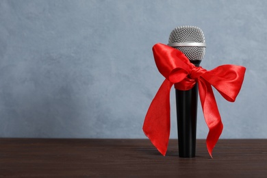 Photo of Microphone with red bow on wooden table against grey background, space for text. Christmas music