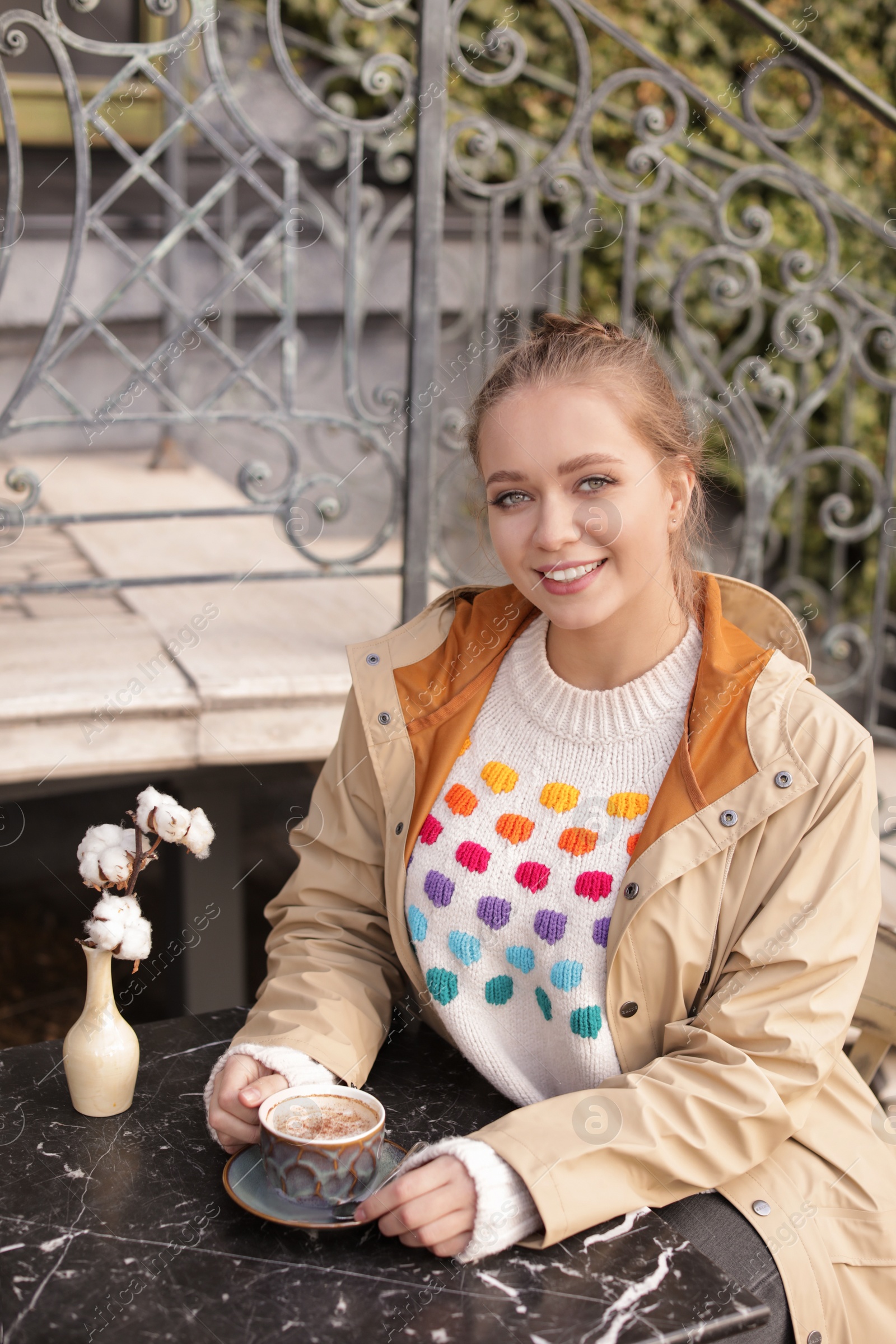 Photo of Young woman enjoying tasty coffee at table outdoors