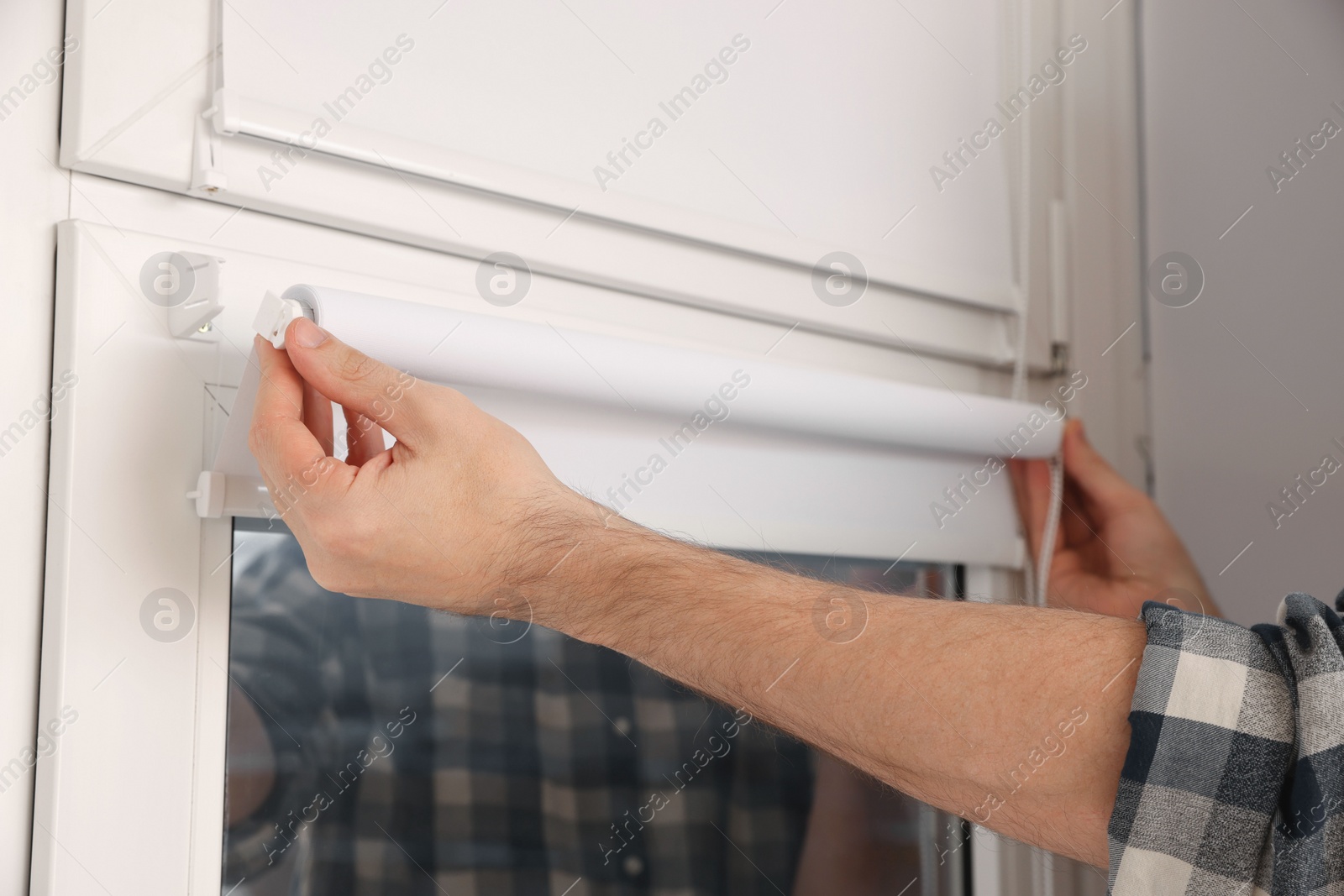 Photo of Man installing roller window blind indoors, closeup