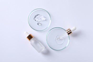 Photo of Petri dishes with samples of cosmetic serums, pipette and bottle on white background, flat lay