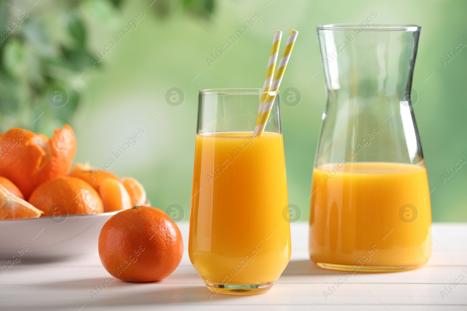 Photo of Delicious tangerine juice and fresh fruit on white wooden table against blurred background