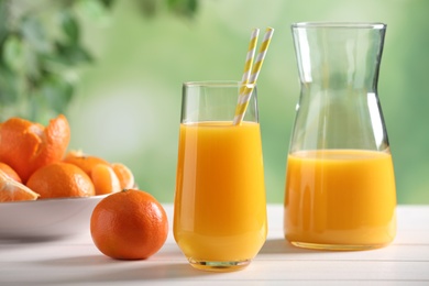 Photo of Delicious tangerine juice and fresh fruit on white wooden table against blurred background