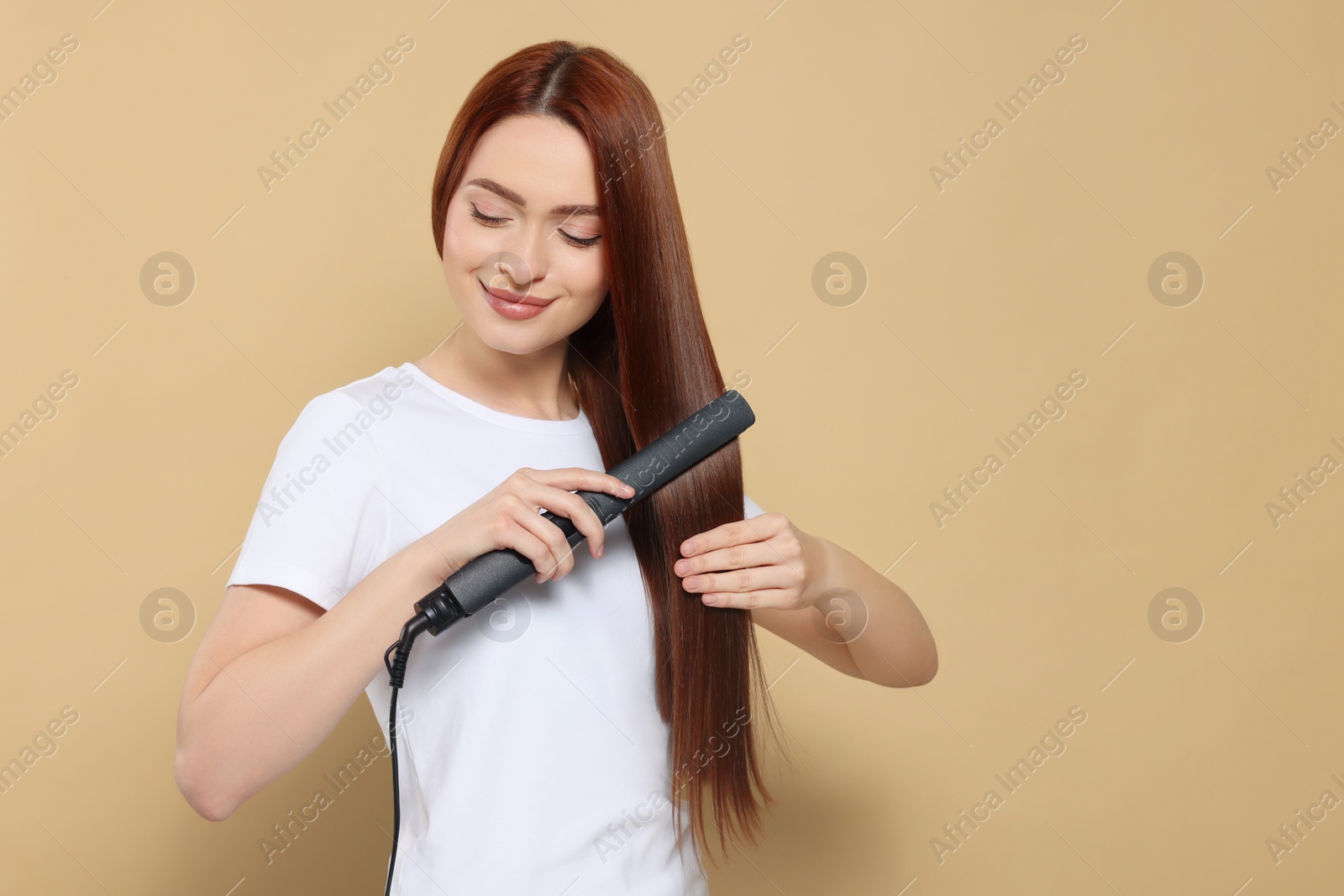Photo of Beautiful woman using hair iron on beige background, space for text