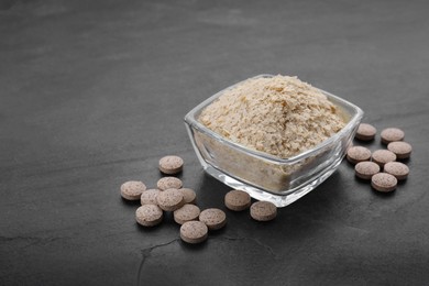 Brewer's yeast flakes and tablets on black table, space for text