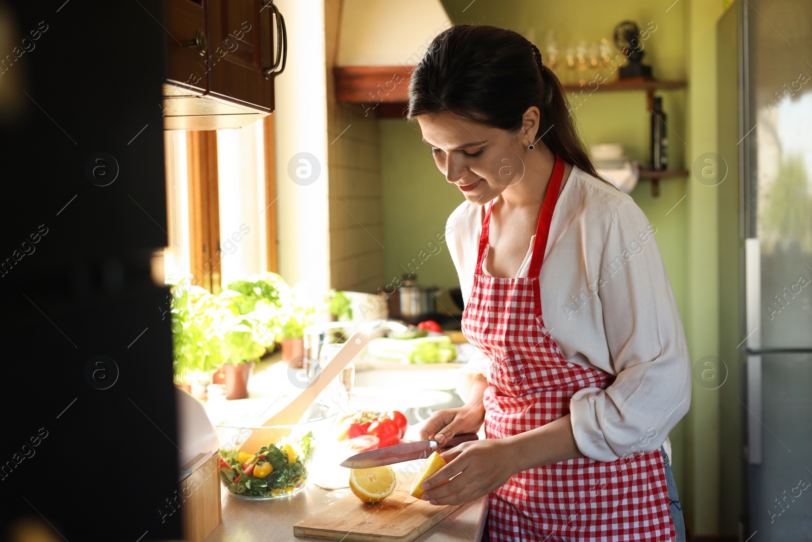 Photo of Young woman cutting fresh lemon at countertop in kitchen