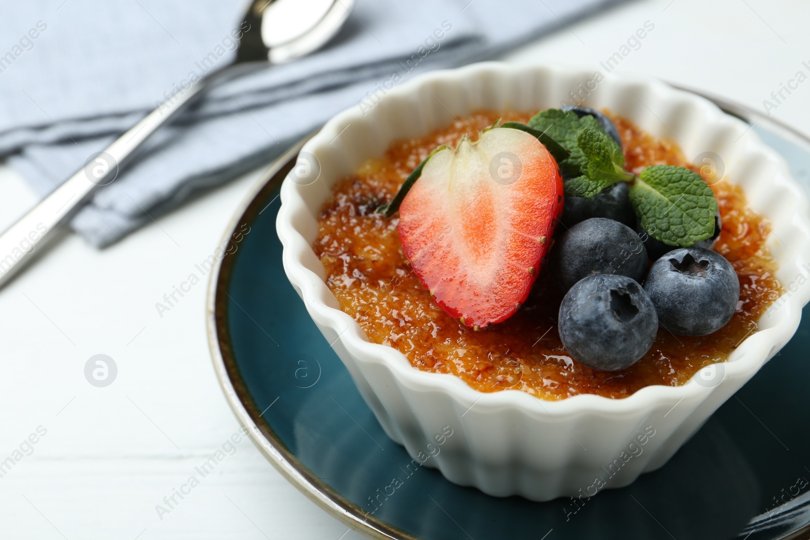 Photo of Delicious creme brulee with berries and mint in bowl on white table, closeup. Space for text