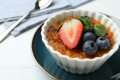 Delicious creme brulee with berries and mint in bowl on white table, closeup. Space for text