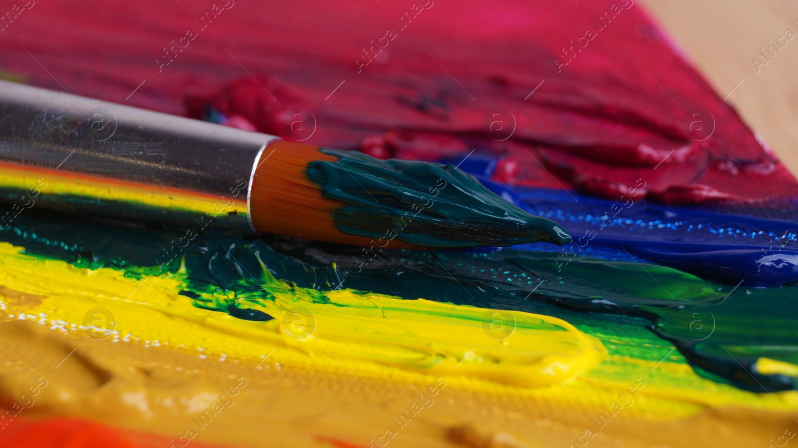 Photo of Brush on artist's palette with colorful mixed paints, closeup