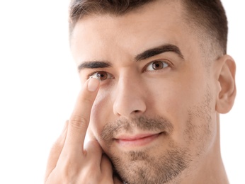 Young man putting contact lens in his eye on light background