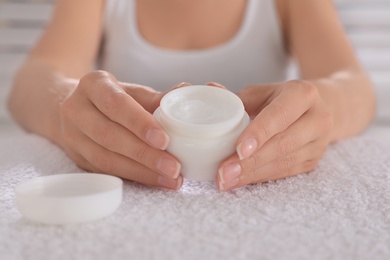 Woman holding jar with cream on white towel, closeup