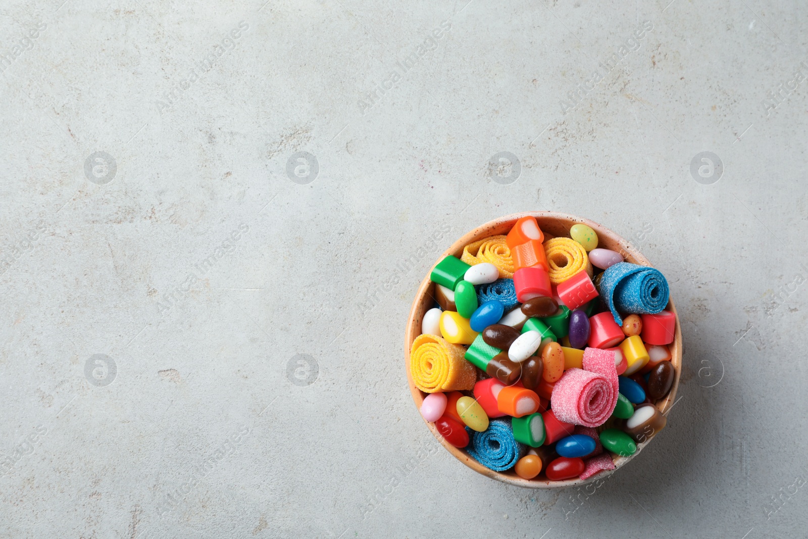 Photo of Bowl of delicious colorful candies on gray table, top view with space for text