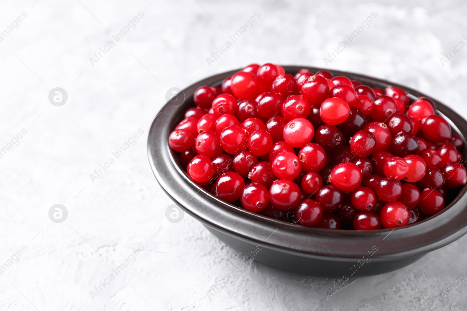 Photo of Fresh ripe cranberries in bowl on grey table, closeup