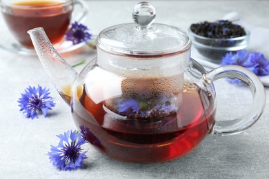 Glass pot with tea and cornflowers on light table, closeup