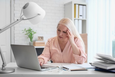 Mature woman suffering from headache while sitting at table in office