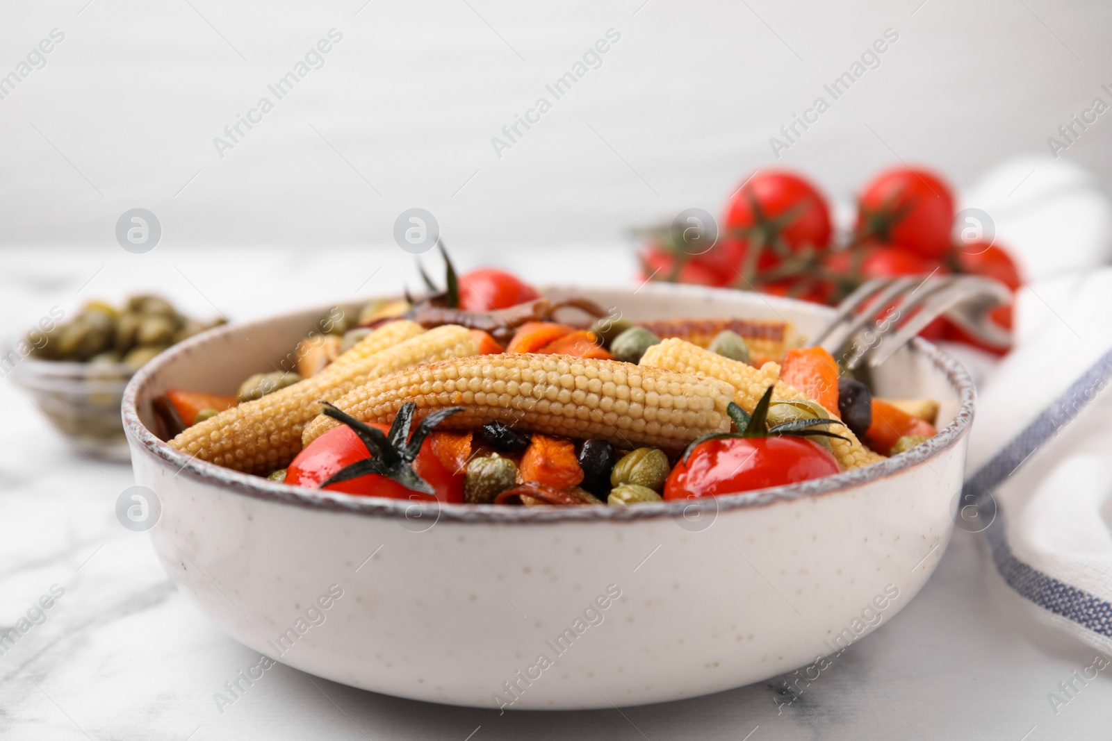 Photo of Tasty roasted baby corn with tomatoes and capers on white marble table, closeup