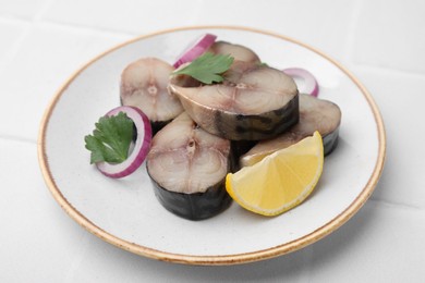 Slices of tasty salted mackerel with lemon and onion on white tiled table, closeup