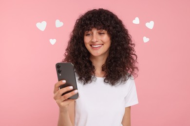 Image of Long distance love. Woman chatting with sweetheart via smartphone on pink background. Hearts around her