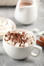 Cup of aromatic hot chocolate with marshmallows and cocoa powder on gray table, closeup