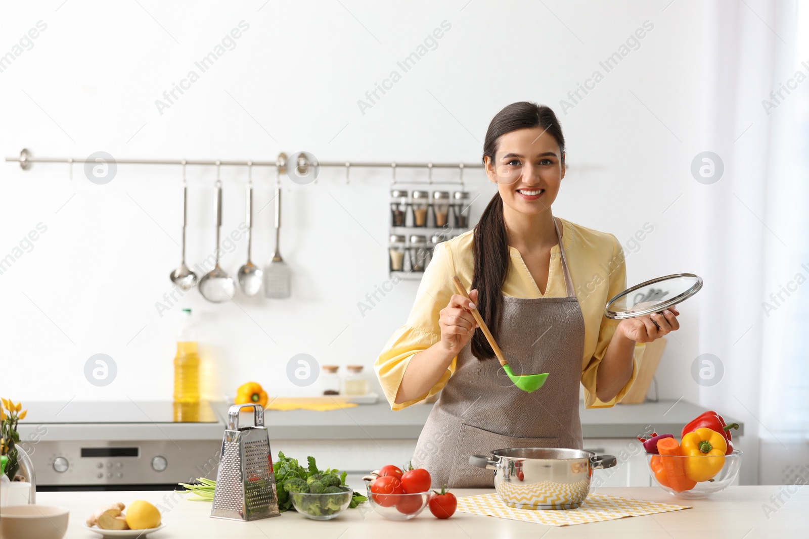 Photo of Young woman cooking tasty soup in kitchen