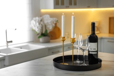 Photo of Pair of beautiful golden candlesticks and wine on white marble table in kitchen, space for text