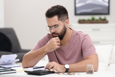 Photo of Worried young man counting money at white table indoors