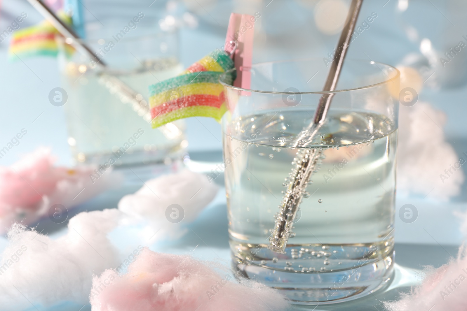 Photo of Tasty cocktail in glass and cotton candy on light blue background, closeup